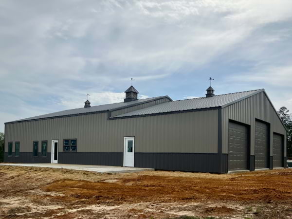 two tone dark grey garage or shop with three size doors for car pull ins and five windows on a dirt area