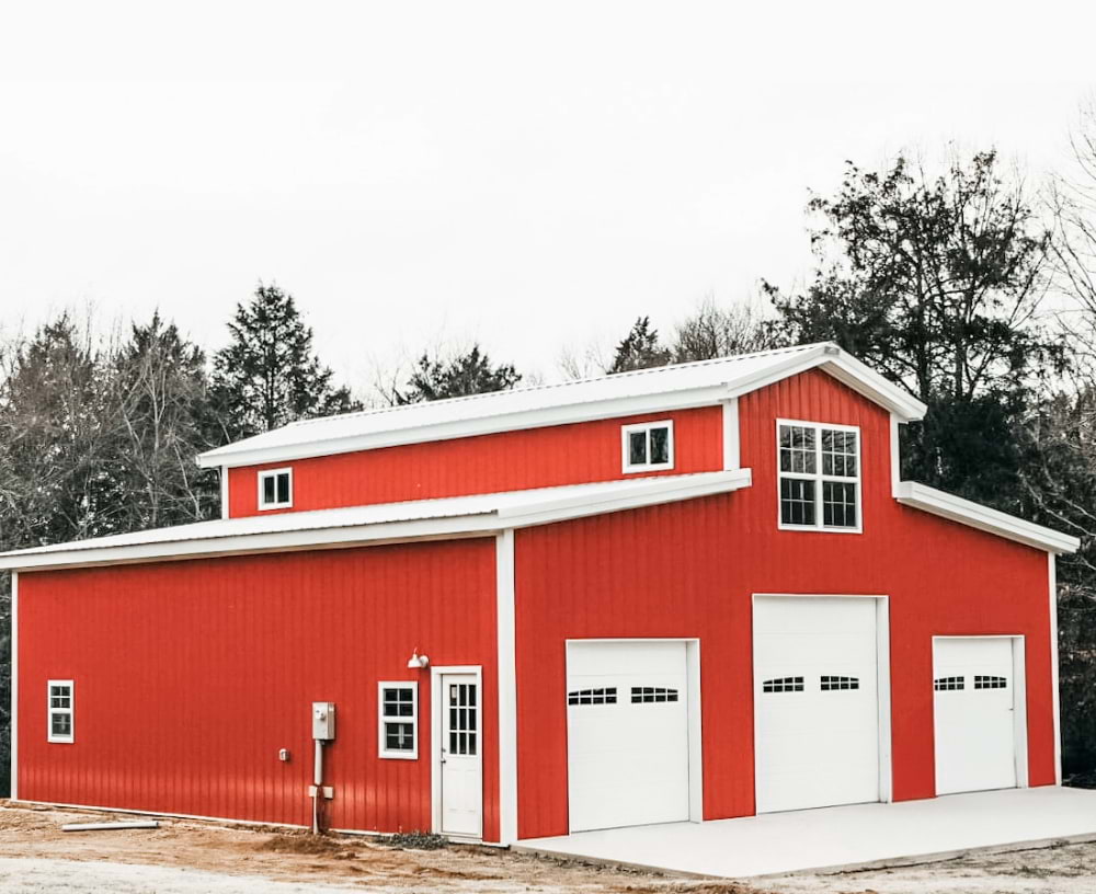 White and red garage ag building with three white garage doors, one personal door and five windows