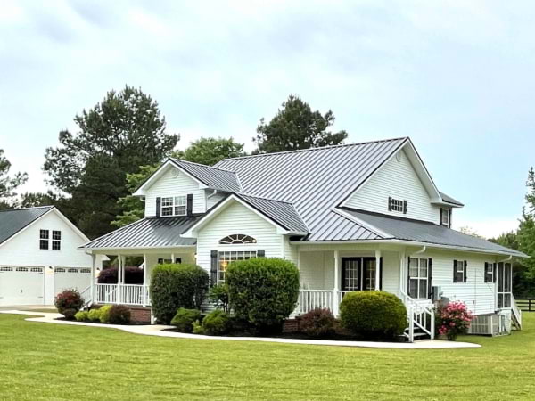 White house with a black metal roof and bushes in the front