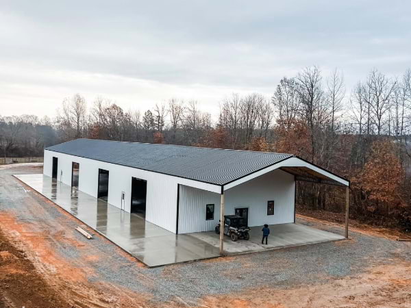 Large white shop with four car doors and a front with a covered area on a concrete pad and gravel area